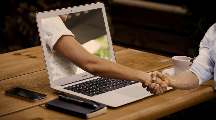 Eine Hand die aus einem Laptop herausragt und einer Person die hand schüttelt
